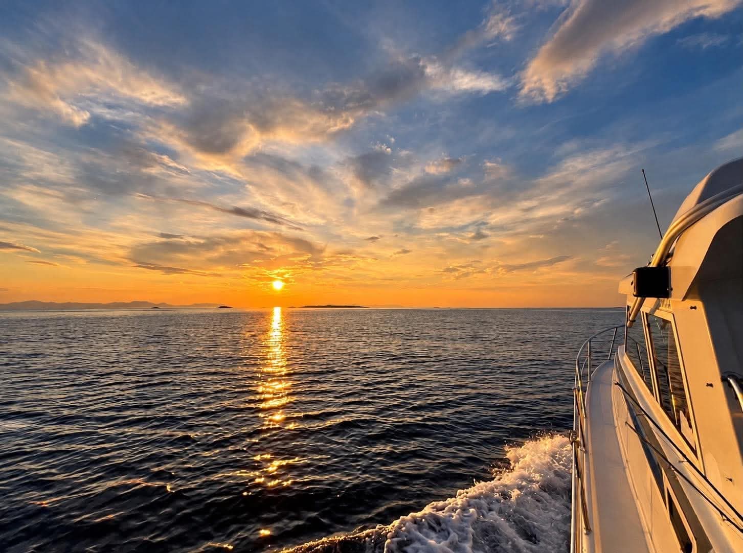 The boat cutting through the sea towards a low sun, islands on the horizon