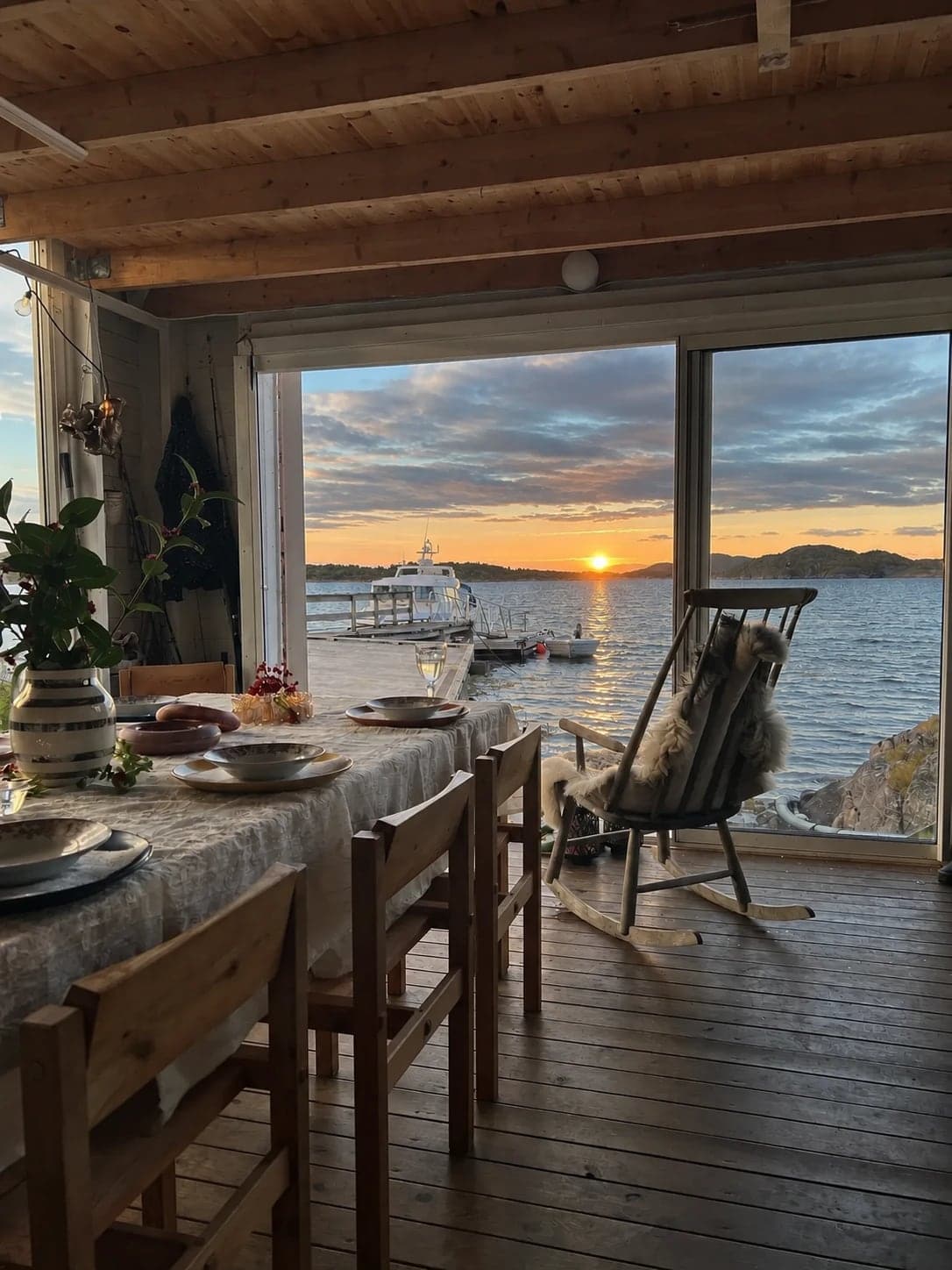 The long table laid in the Sea Lodge, a sheepskin on the rocking chair and the sun going down over the dock