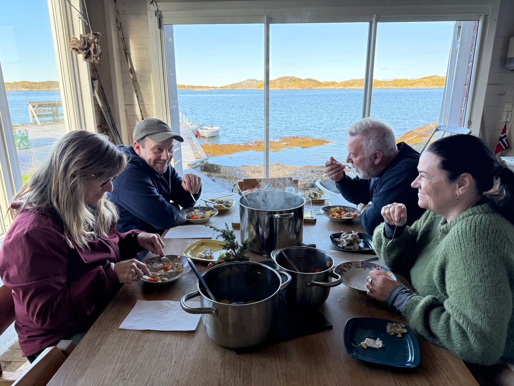 Four guests eating together around the Sea Lodge table, the fjord through the window