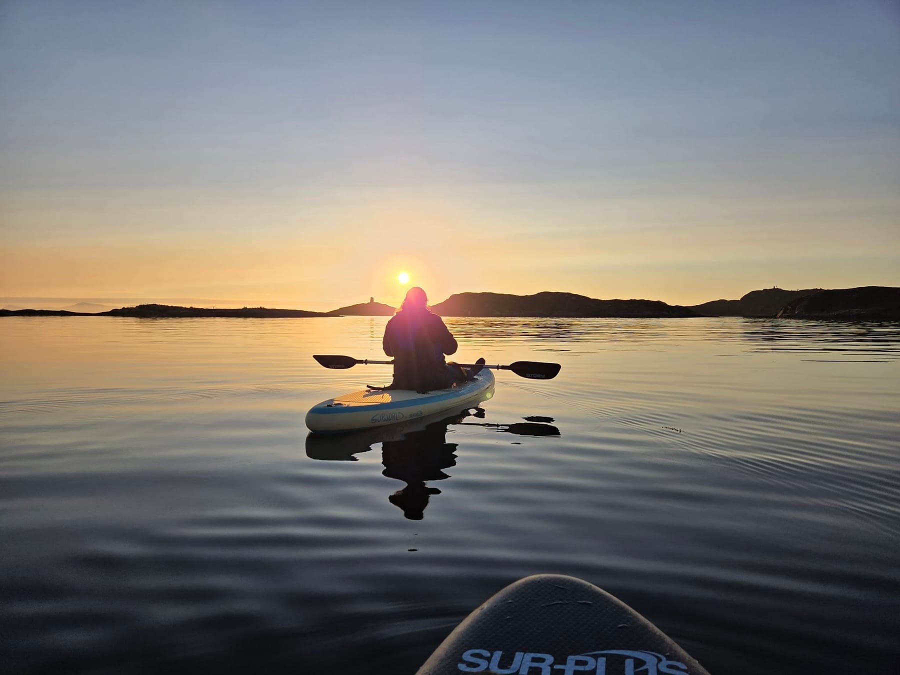 A paddler heading into the low sun on mirror-flat water