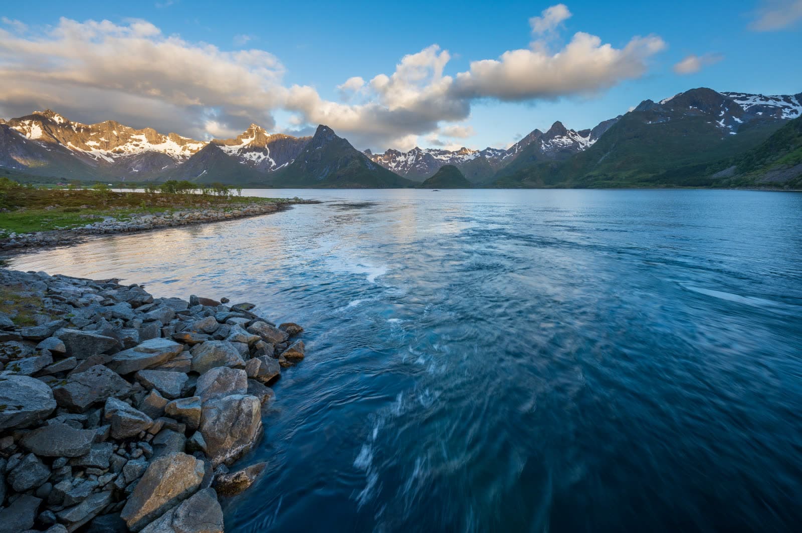 The tide running into a fjord in Hadsel, Vesterålen, a stony shore in front and sharp peaks beyond