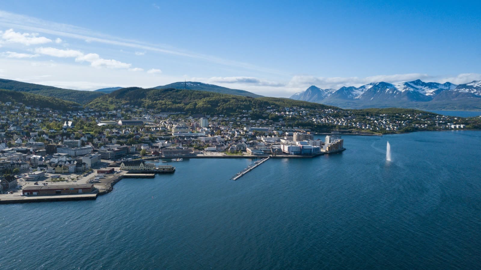 Harstad from the air on a clear day, the harbour and the town by the fjord and snow-capped mountains beyond