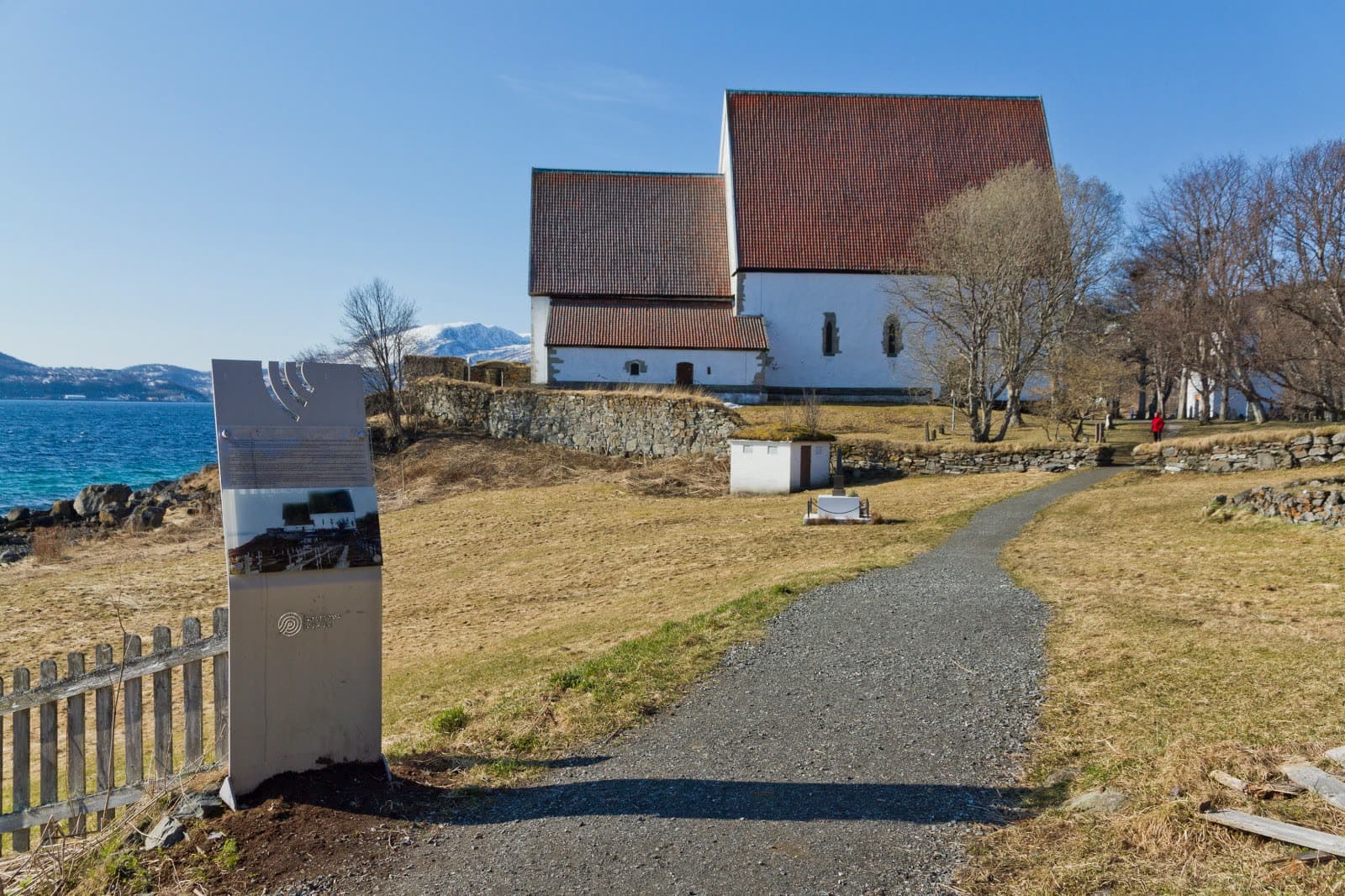 Trondenes Church, white stone walls under a red roof, the path through the churchyard and the sea behind