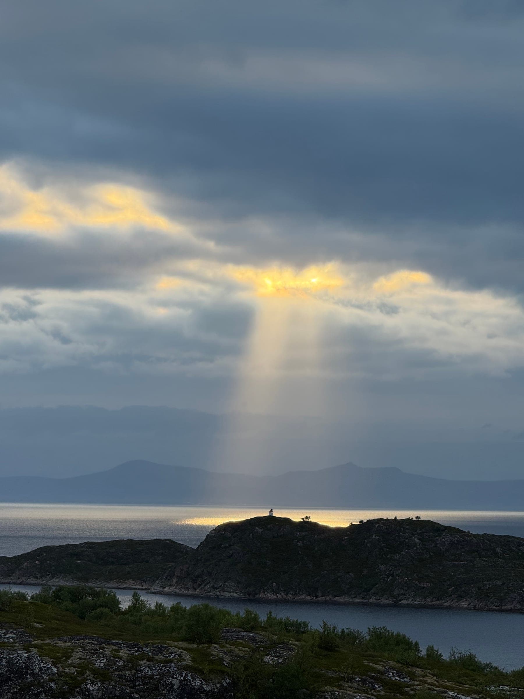 A shaft of evening light breaking through cloud onto a lone islet and its lighthouse