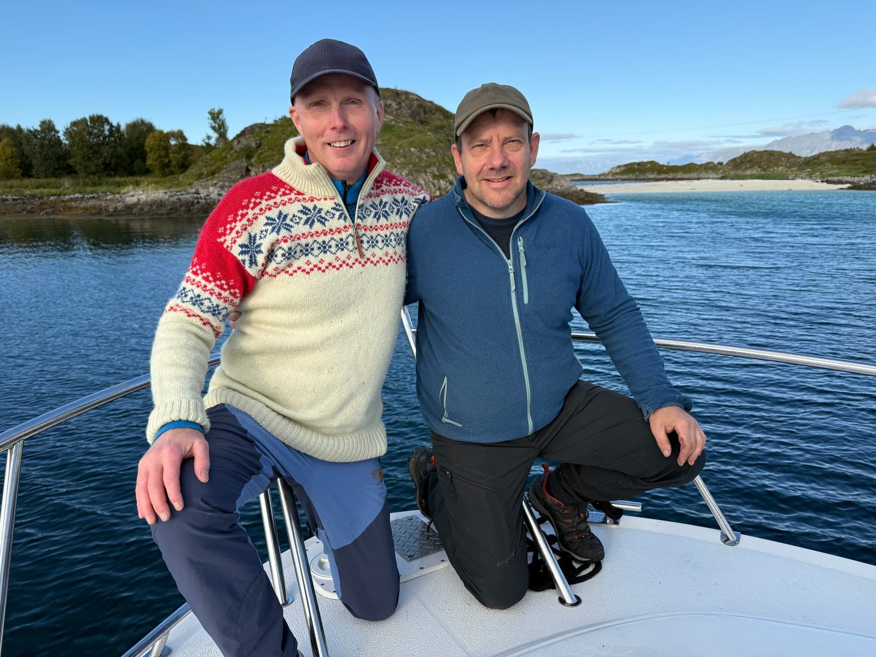 Raymond and Eirik on the bow of their boat, the island and a white beach behind them